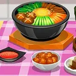 분홍색 체크 무늬 테이블보 위에 다양한 음식이 담긴 그릇과 접시들, 김치, 국, 두부 요리가 놓여 있다