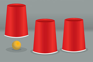 빨간 컵 세 개가 거꾸로 놓여 있고, 하나의 컵 앞에 노란 공이 있습니다