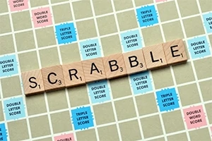 가로로 놓인 나무 블록에 SCRABBLE이라는 글자가 써 있고, 점수가 표시된 바둑판 무늬의 게임 보드 위에 놓여있다